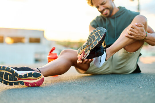 Portrait of a young man sitting with a leg injury in pain, after running or exercising in city street outdoors