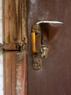 A detailed close-up shot of a weathered and damaged entrance door. The brown faux leather upholstery is torn open, revealing the foam padding underneath, while the metal plate and handle show signific