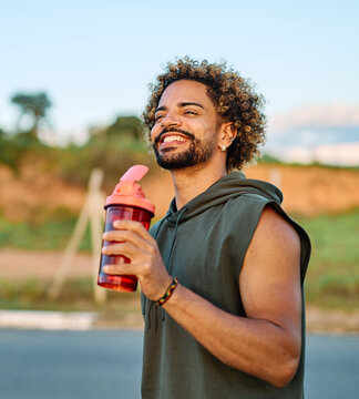 Portrait of a happy man holding a bottle of water refreshment posing and smiling after exercicing outdoors. Athlete and fitness and healhty living concept