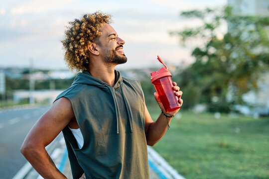 Portrait of a happy man holding a bottle of water refreshment posing and smiling after exercicing outdoors. Athlete and fitness and healhty living concept