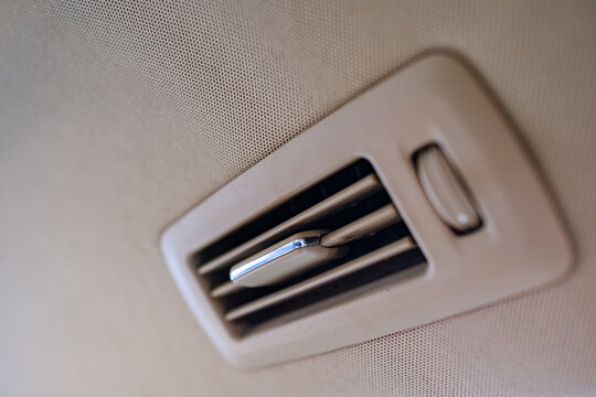 Air conditioning climate control vent mounted on the beige fabric ceiling headliner inside a luxury car passenger compartment