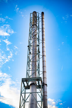 Industrial metal smokestack and exhaust pipe against bright blue sky