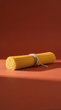Vertical perspective of raw spaghetti pasta package tied with string against warm terracotta backdrop