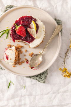 Partially eaten mini cheesecake with berry jam lemon and strawberry served on a ceramic plate