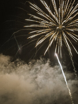 Brilliant white fireworks exploding in the dark night sky with smoke clouds below during a grand celebration