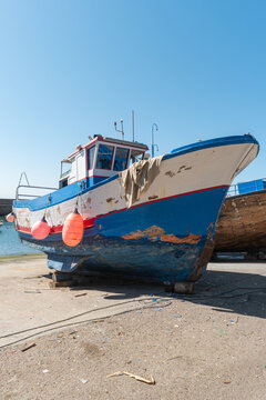 Old weathered blue and white fishing boat hauled out on the dry dock for maintenance and repair work under a clear sky