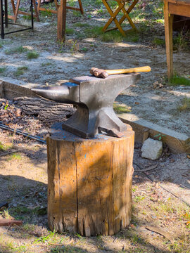 Blacksmith anvil resting on a wooden log outdoors with a hammer placed on top ready for metalworking crafts and traditional blacksmithing work