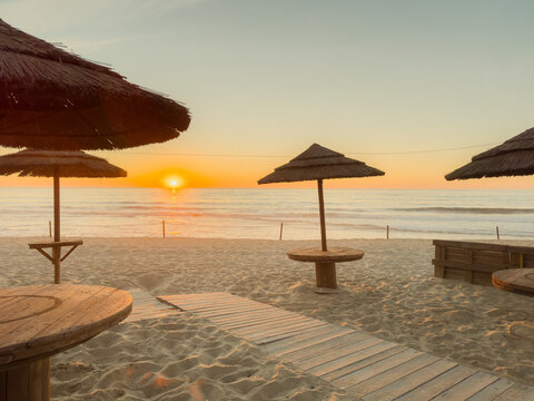 Sunset beach view with straw umbrellas and wooden pathway