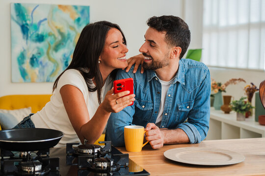 An intimate breakfast moment captures a grateful couple sharing a smile as a vibrant red phone becomes the focal point on a sunlit counter, warm mugs, and cheerful conversation. Fresh energy in air