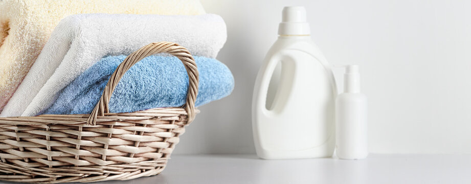 Stacked pastel towels in wicker basket beside laundry detergent bottle on white countertop linen set