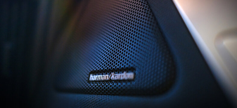 Macro view of Harman Kardon badge on metallic speaker grille cover of automotive high fidelity sound system in car interior