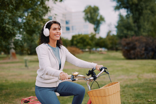 Young woman enjoying a bike ride in the park, listening to music with headphones, embracing an active and happy lifestyle outdoors