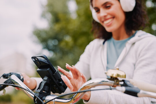 Woman cycling outdoors, interacting with a mounted smartphone for navigation or music selection while wearing headphones, smiling and enjoying active leisure time
