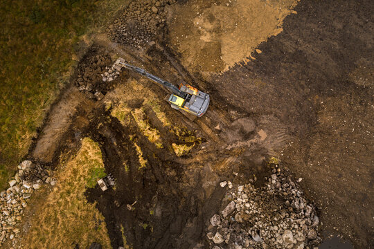 Aerial view of an excavator working in a muddy field with piles of rocks and excavated soil, Jaeren, Norway.