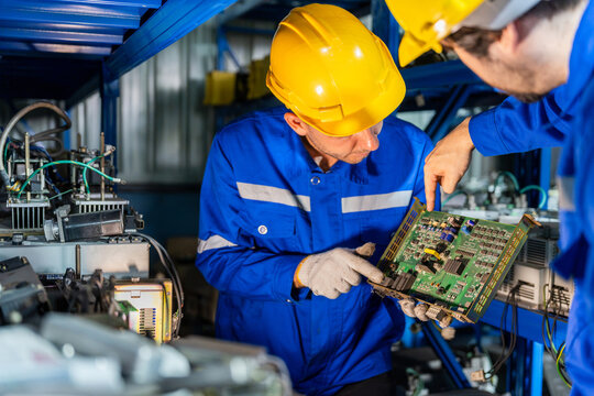 Industrial engineers inspecting electronic circuit board in factory warehouse, technicians checking electronic equipment and pointing at part in manufacturing plant