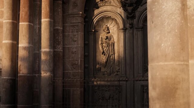 Quito, Ecuador. Sunlight glows softly on ancient stone carvings. Statue of a saint stands serene within grand archway. Columns frame the scene, bathed in quiet reverence.