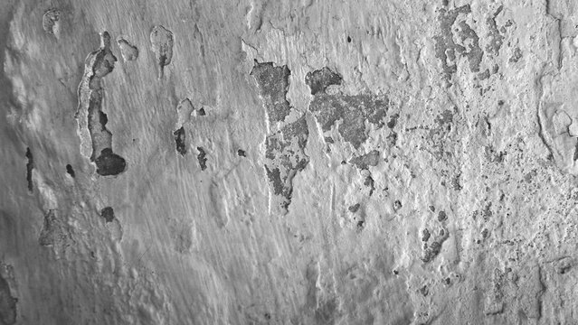 Monochrome close-up of chipped white paint and exposed gray plaster on an aged wall, featuring rough edges, cracks and weathered surface details.