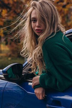 Young woman in green sweater enjoying autumn breeze by a car