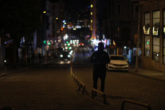 Silhouette of Person on Nighttime Urban Street with Blurred City Lights