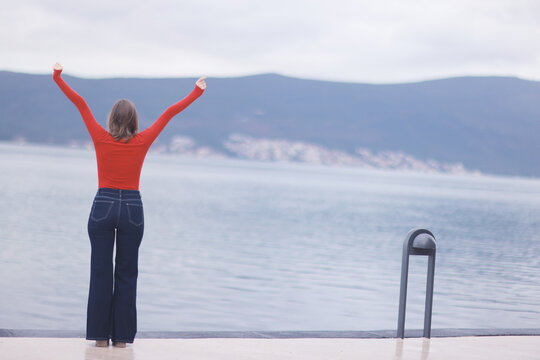 Joyful Woman Celebrating at Tranquil Lakeside in Red Top and Jeans