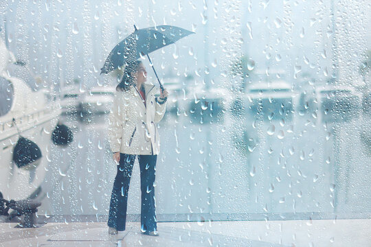 Woman with Umbrella Stands Amidst Raindrops on Glass Overlooking Foggy Marina