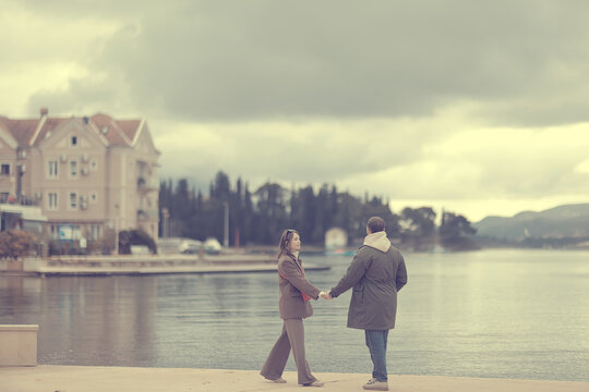 Couple Holding Hands by Tranquil Waterfront Under Overcast Sky