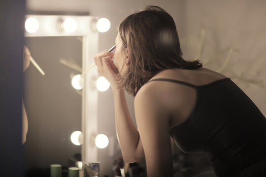 Woman Applying Makeup in Front of Illuminated Mirror for Evening Glamour