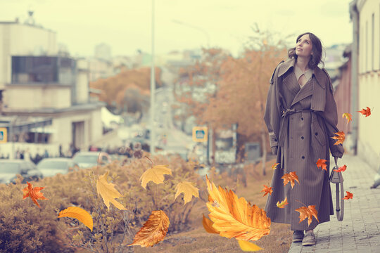 Fashionable Woman in Autumn Coat Strolling Through Cityscape with Falling Leaves