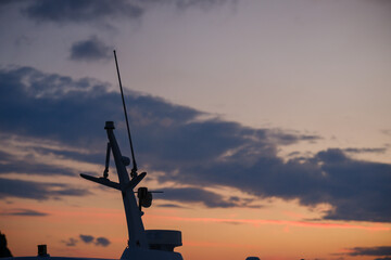 Boat navigation antenna and mast equipment standing tall against a glowing orange twilight horizon with evening clouds at sea © Bugra Kaan Ersoy