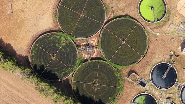 Aerial view of circular sedimentation tanks at a water treatment facility with industrial infrastructure and surrounding dry landscape in St Neots, England, United Kingdom.