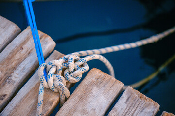 Mooring rope tied in secure knot on weathered wooden pier planks over deep blue sea water, maritime marine dock detail at harbor © Bugra Kaan Ersoy