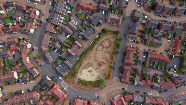 Aerial view of a modern residential housing estate with rows of houses, paved streets, parked cars, and a central green space in Bedford, England, United Kingdom.