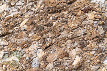Obraz premium Rough brown conglomerate rock surface with mixed stone fragments
