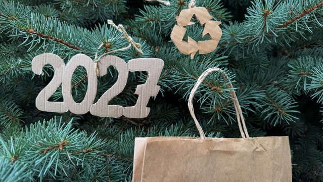 Paper shopping bag on pine tree next to 2027 numbers and recycle sign, eco friendly holiday delivery, christmas spirit.