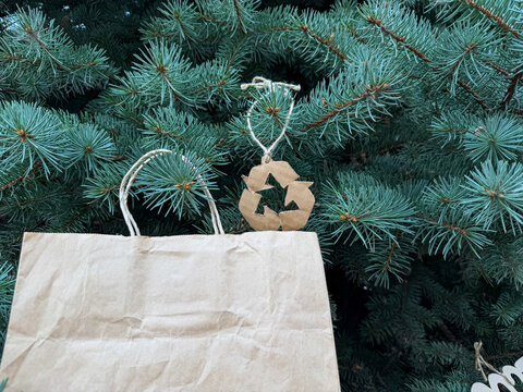 Craft shopping bag hanging on pine branches with recycling emblem, green holiday delivery, eco friendly christmas.