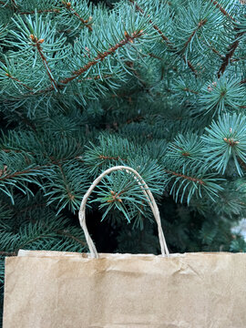 Vertical view of paper bag on evergreen fir branches, eco friendly holiday shopping, sustainable packaging concept.