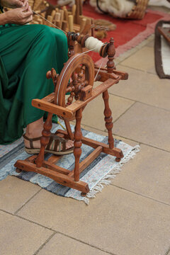 Woman creating textile thread from raw wool on a vintage spinning wheel, demonstrating old craft techniques