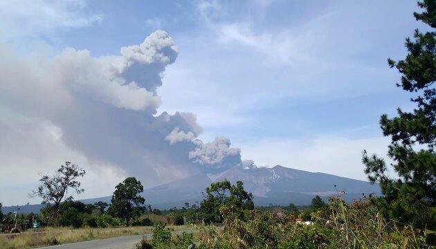 Volcano erupting with smoke and ash plumes against a blue sky.