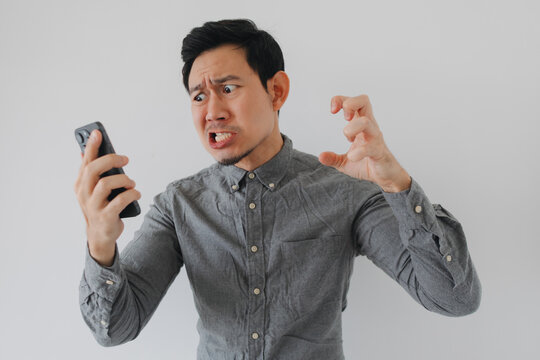 Angry Asian man reacting to bad news on his smartphone with a frustrated expression.