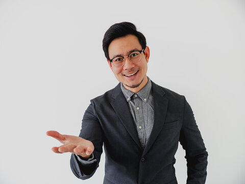 Smiling Asian businessman in suit presents with open hand on white background.