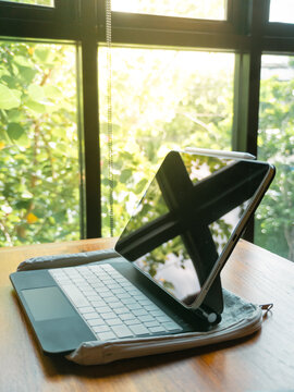 Modern tablet with keyboard and stylus on a wooden table by a bright window.