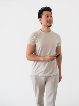Thoughtful Asian man in casual attire holding a device, looking up with a slight smile.