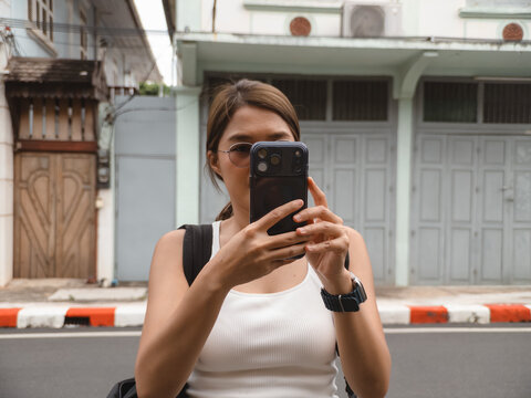 Young woman traveler capturing street scene with smartphone, exploring historic urban architecture during daytime.