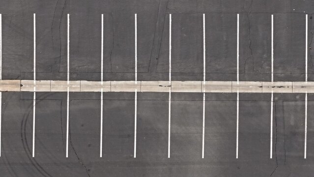 Aerial view of an empty asphalt parking lot with white painted parking space lines and a concrete divider in Boulder, Colorado, United States.