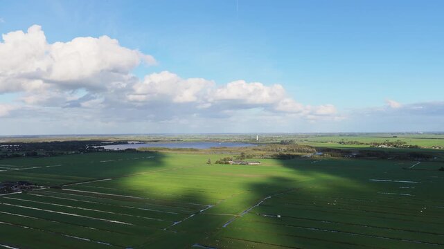Aerial drone view of polders and agricultural fields in the Netherlands. Rural landscape with canals and cloud shadows under a blue sky.
