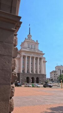 Sofia, Bulgaria - 16.06.2025, View of former Communist Party House spire framed by stone colonnade arcade of National Assembly building in Largo architectural ensemble, sunny day perspective, vertical