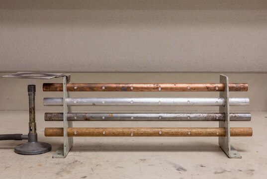 Thermal conductivity experiment demonstrating heat transfer rates in copper, aluminum, iron, and wood rods using melting wax drops on a lab bench.
