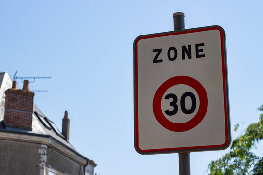 Traffic sign indicating a 30 km/h speed limit in a residential area with buildings and clear blue sky in the background