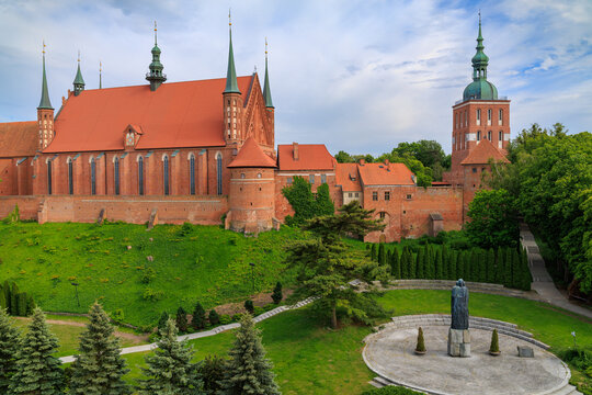 Historic Frombork Cathedral complex with red brick walls, green spires, and surrounding park on a cloudy day in Poland