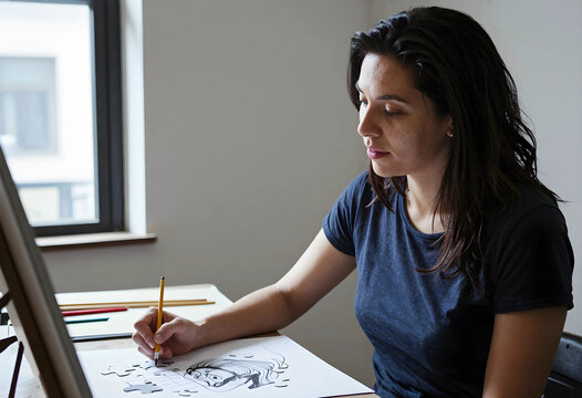 Creative process and artistic inspiration, woman drawing a puzzle sketch with a pencil at a desk in a home studio for design and illustration projects